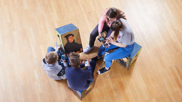 Vier Jugendliche betrachten ein Porträt Martin Luthers auf einem Hocker.