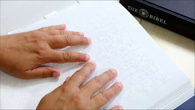 Eine blinde Frau liest eine Bibel in Brailleschrift