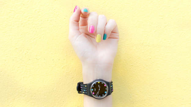 Hand mit bunt lackierten Fingernägeln und Armbanduhr am Handgelenk