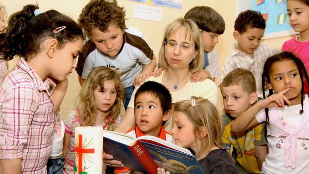 Kita-Kinder der Antoniusgemeinde Frankfurt lesen mit ihrer Erzieherin in einer Kinderbibel