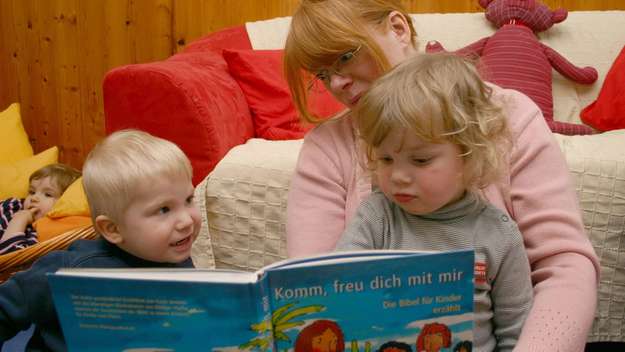 Eine Erzieherin liest Kleinkindern aus einer Kinderbibel vor