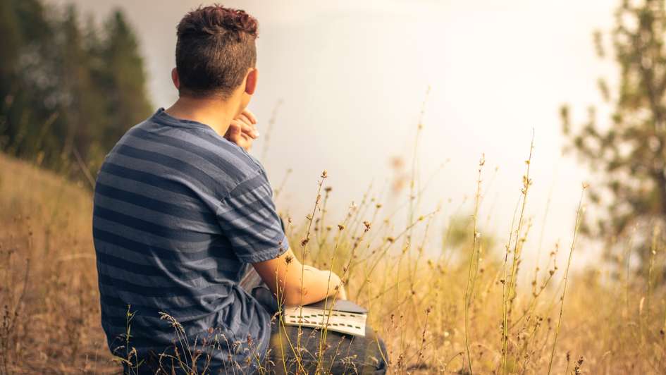 Symboldbild: Ein Mann hält eine Bibel auf dem Schoß und betrachtet die Landschaft