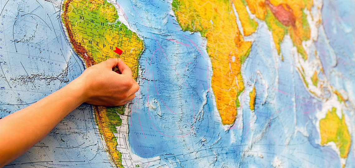 hand with apin in front of a world map.