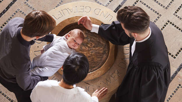 Ein Pfarrer tauft einen Säugling, der von seinen Eltern über das Taufbecken gehalten wird. Ein Pfarrer tauft einen Säugling, der von seinen Eltern über das Taufbecken gehalten wird.