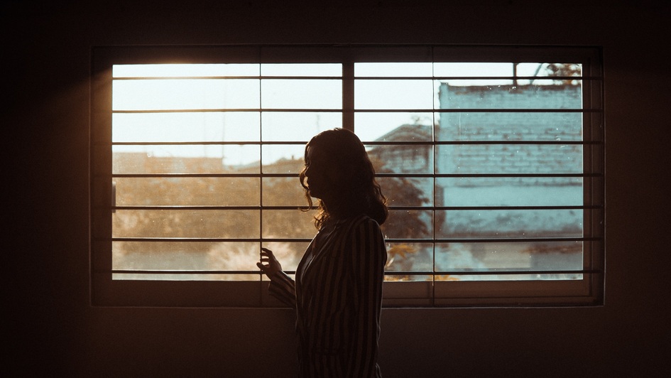 Eine Frau steht in einem dunklen Raum am Fenster Eine Frau steht in einem dunklen Raum am Fenster