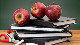 Bücher, Schere, Kreide und ein Apfel vor einer Tafel