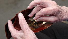 Gealterte Hände greifen in eine Geldbörse mit Münzen