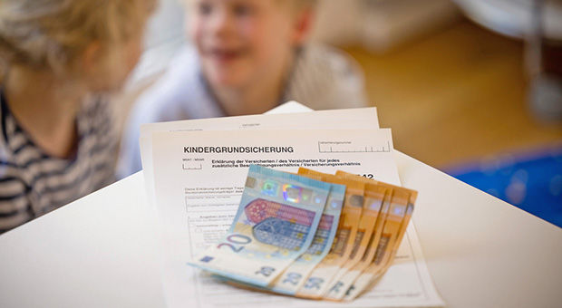 Formular Kindergrundsicherung mit Geldscheinen auf dem Tisch/Kinder im Hintergrund