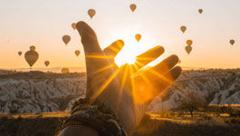 Hand  in aufgehender Sonne und Heißluftballons im Hintergrund