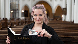 Junge Frau in einer Kirchenbank mit Leselupe und Bibel