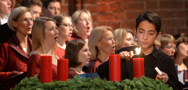 Ein Junge zündet die erste Adventskerze an. Im Hintergrund singt der Kirchenchor