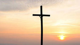 Kreuz mit aufgehender Sonne im Hintergrund