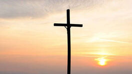 Kreuz mit aufgehender Sonne im Hintergrund