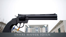 Attrappe einer Pistole und dem Slogan "Unsere Waffen Töten"