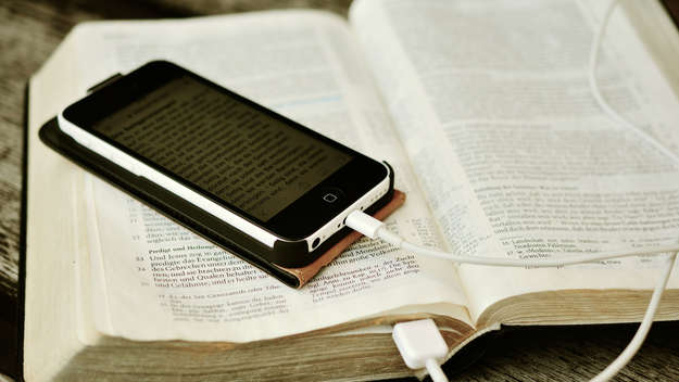 Smartphone liegt mit Ladekabel auf einer Bibel