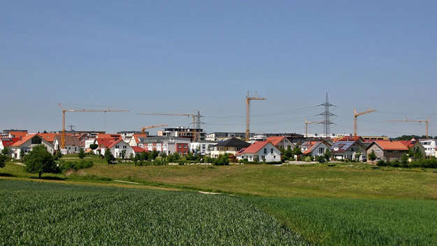 Neubaugebiet mit Baukränen und im Vordergrund Feld