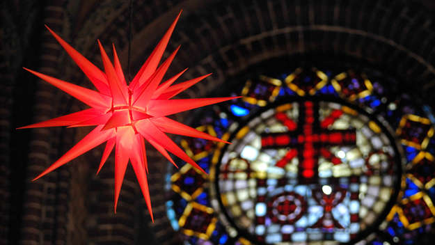 Ein Herrnhuter Stern in Rot vor einem bunten Kirchenfenster