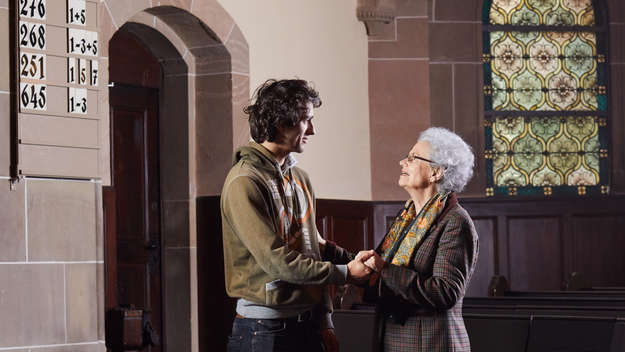 Ein junger Mann steht mit einer älteren Frau in einer Kirche und hält ihre Hand.