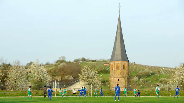 Fußballer spielen auf einem Sportplatz vor der Kulisse der evangelischen Kirche Oberöwisheim.