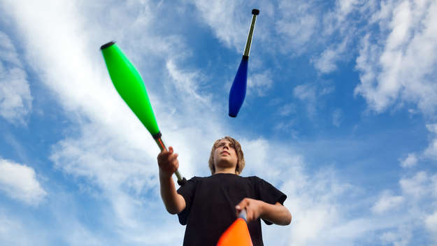 Ein Junge jongliert mit drei Keulen vor blauem Himmel.