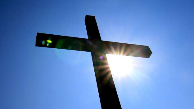 Kreuz im Gegenlicht vor blauem Himmel