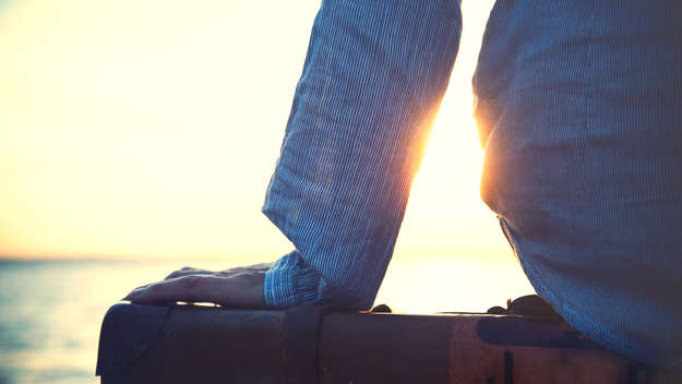 Person sitzt auf einem Koffer und blickt in einen Sonnenuntergang.