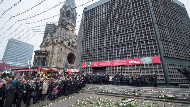 Vor der Kaiser-Wilhelm-Gedächstniskirche in Berlin stehen viele Menschen und gedenken der Opfer des Anschlags am Breitscheidplatz 2016. Am Boden liegen weiße Blumen.