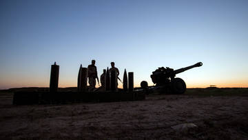 Silhouette von Soldaten und Artilleriegeschütz im Gegenlicht vor Abendhimmel