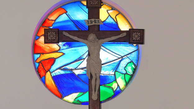 Kreuz vor farbigem, runden Kirchenfenster
