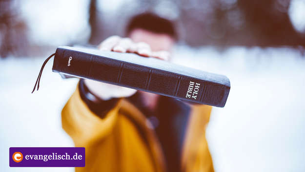 Jugendlicher hält eine Bibel vor sein Gesicht