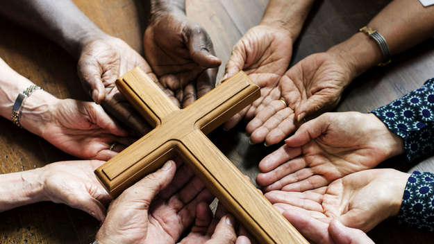 Mehrere Hände unterschiedlicher Hautfarbe halten ein Holzkreuz