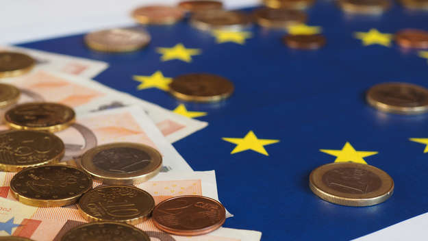 Euro-Münzen und Geldscheine liegen auf einer EU-Flagge.