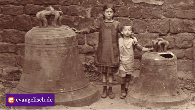 Ein Mädchen und ein Junge stehen neben zwei Kirchenglocken