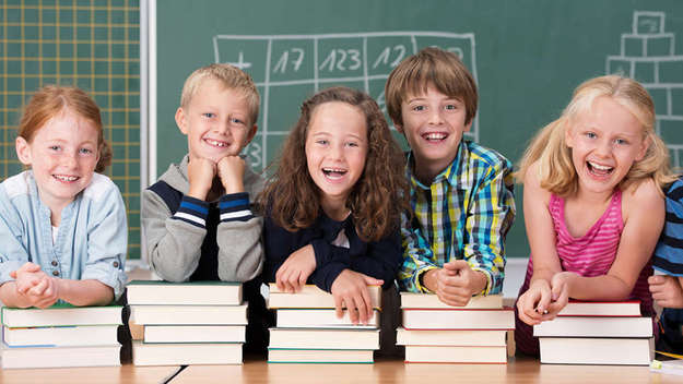 Lachender Kinder mit Schulbüchern vor einer Tafel