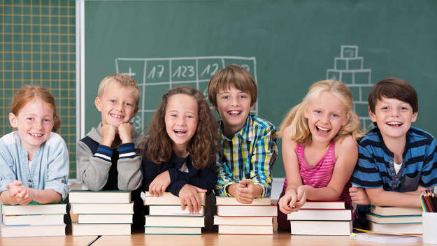Lachende Kinder mit Stapeln an Büchern vor einer Schultafel