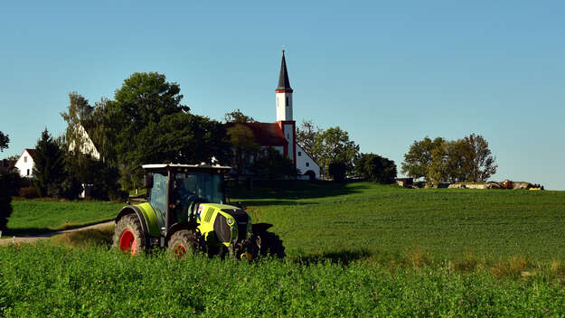 Traktor auf dem Feld, im Hintergrund ein Kirchturm