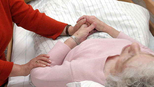 Eine ehrenamtliche Sterbebegleiterin sitzt am Bett einer kranken Pflegeheimbewohnerin.