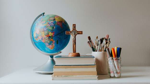 Schreibtisch mit einem Globus, einem Kreuz, Büchern und Stiften darauf