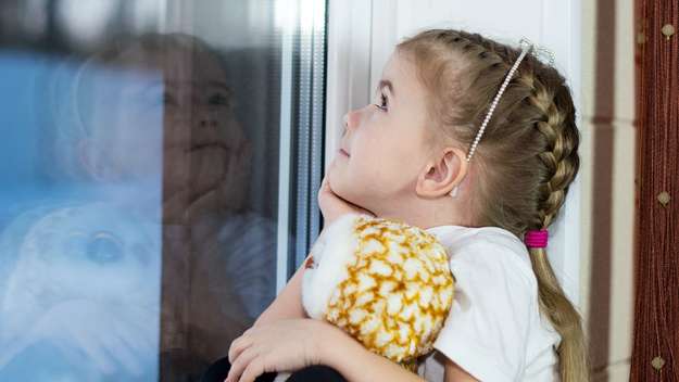 Mädchen hält ein Kuscheltier und schaut aus dem Fenster