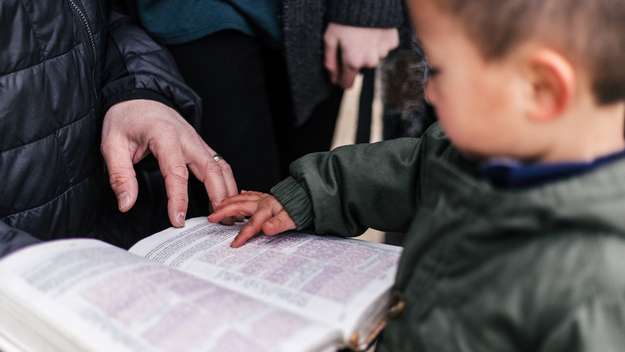Junge zeigt auf eine Bibel