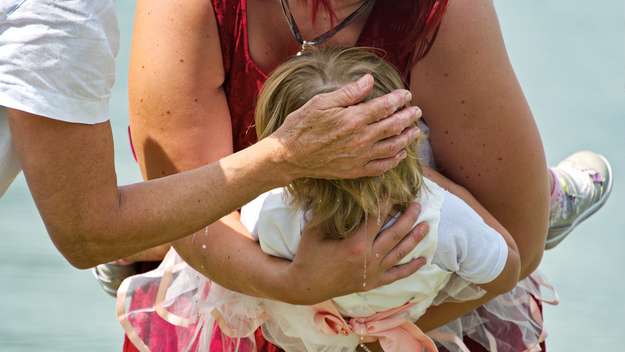 Mutter hält Tochter bei Taufe im See auf dem Arm