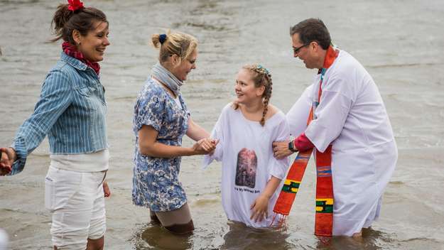 Mädchen wird von einem Pfarrer in der Elbe getauft