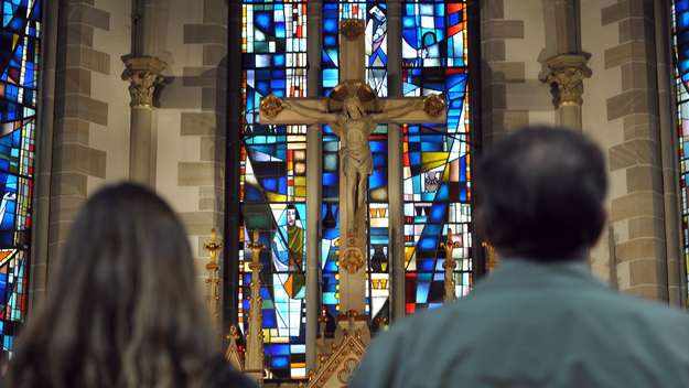 Frau und Mann stehen in der Gartenkirche St. Marien in Hannover vor dem Kreuz