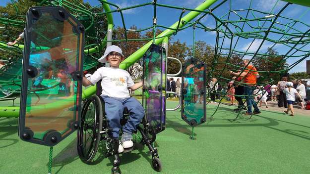 Inklusiver Spielplatz in Bremen: Vor einem Klettergerüst sitzt ein lachender Junge in einem Rollstuhl.