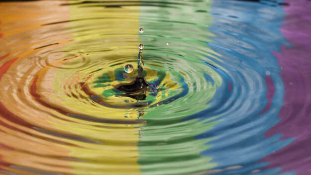 Symbolbild für Frieden: Ein regenbogenfarbener Wassertropfen fällt ins Wasser