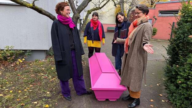 Vier Frauen stehen um einen rosa Sarg