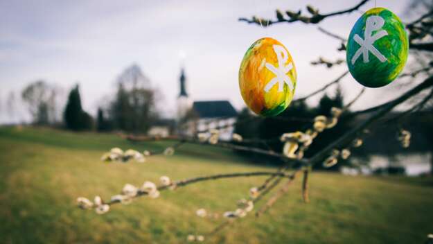 Bemalte Ostereierschalen in einem Baum vor einer Kirche