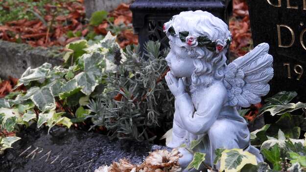 Ein Engel mit Rosenkranz sitzt auf einem Grab des Friedhof II der Sophiengemeinde Berlin.