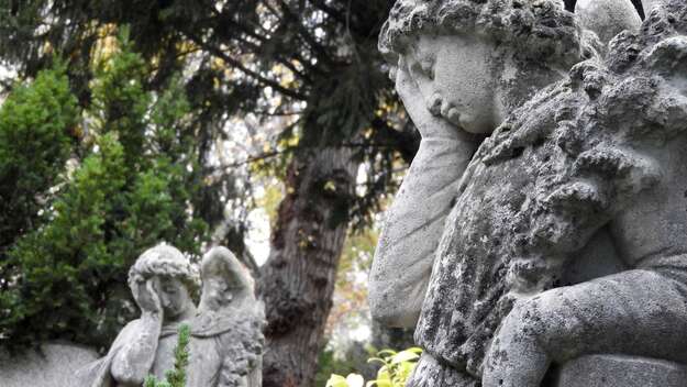 Ein Engel mit Rosenkranz sitzt auf einem Grab des Friedhof II der Sophiengemeinde Berlin.