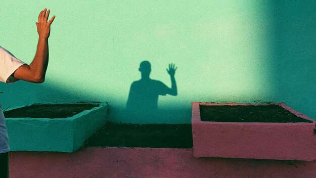 Ein Mann hebt eine Hand. Er ist nur halb zu sehen, doch an der Wand ist sein Schatten sichtbar.